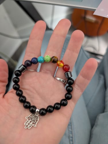 Customer's hand holding a beaded crystal bracelet with black beads, colorful chakra stones, and a silver Hamsa charm.