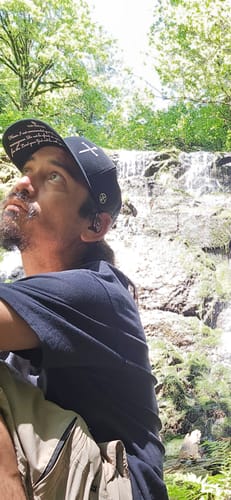 Close-up of a reviewer wearing the black 3 Nail Cross Hat, showing the Joshua 1:9 prayer print on the brim.