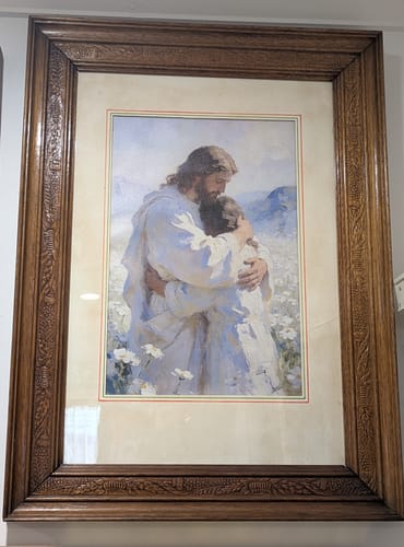 Customer's Jesus' Tender Embrace art print in a carved wood frame, showing the tender embrace in a field of white flowers.