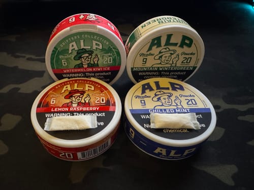 Reviewer's four tins of ALP nicotine pouches in various flavors, showing the pouch shape and size.