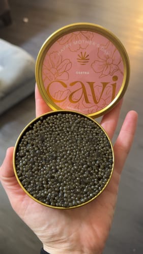 Customer holding an open tin of Osetra Caviar filled with dark pearls, showing the pink limited edition lid.