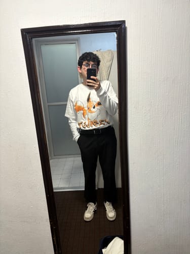 Cliente posa en un espejo de cuerpo entero llevando la camiseta blanca de manga larga Evolution 133 con pantalones negros.