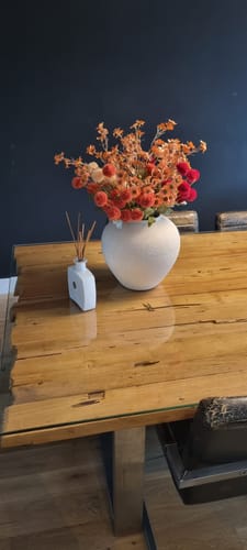 Klant toont de crèmekleurige Sena vaas gevuld met oranje droogbloemen op een houten tafel.