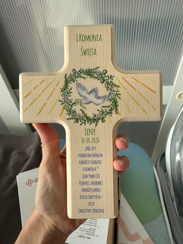 Rezensent hält das personalisierte Holzkreuz mit einem Kranz- und Taubenmotiv in der Hand.