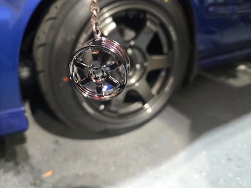 Customer's shiny TE Wheel Keychain hanging in front of a full-size car wheel for scale.