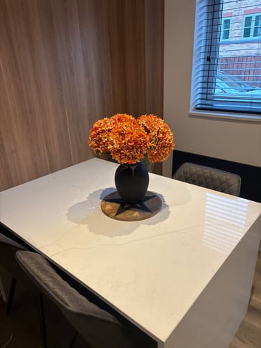 Customer's vibrant orange Faux Hydrangeas in a black vase on a white kitchen table.