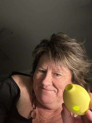 A reviewer holds the yellow Lem Clitoral Massager, showing its green power light.