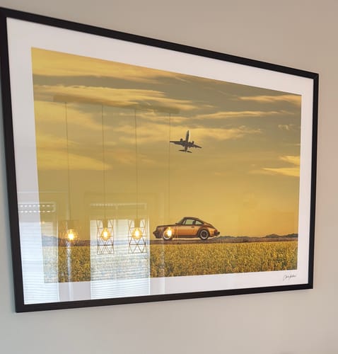 Reviewer's framed art print hanging on a wall, showing an orange car in a yellow field and an airplane.