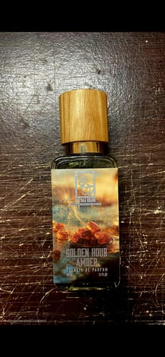 Customer's bottle of Golden Hour Amber perfume with a wooden cap on a dark table.