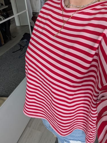 Kundin zeigt den rot-rosa gestreiften Sweater BLOCKSTRIPES, der lässig über einer Jeans getragen wird.