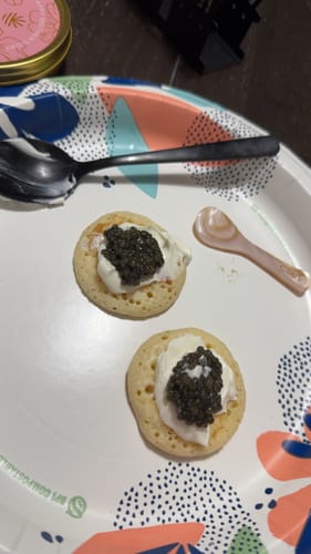Reviewer's pink Mother of Pearl Caviar Spoon on a decorative plate next to two blinis with caviar.