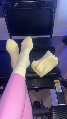 Reviewer's Butter Yellow Waffle Pouch Bag resting on Pilates equipment next to their feet in yellow socks.