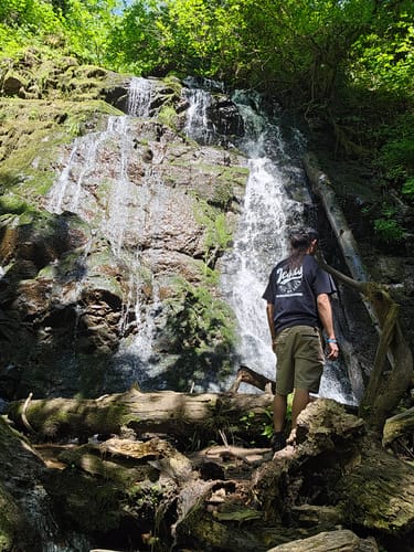 Customer wearing the Jesus Has My Back T-Shirt while enjoying a scenic waterfall view.