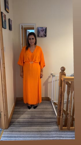Reviewer standing in a hallway, wearing the bright orange Avery Front Slit Dress.