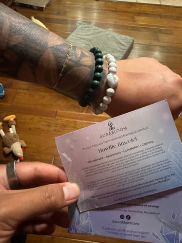 Customer wearing a white beaded Howlite bracelet on a tattooed arm, holding the product information card.