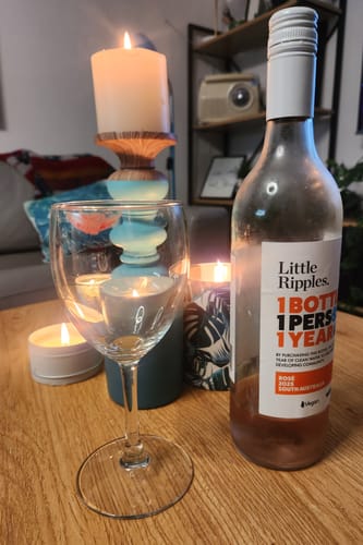 Customer's bottle of Little Ripples Rosé on a candle-lit table next to an empty wine glass.