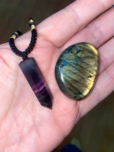 Reviewer's hand holding a purple fluorite necklace and a polished labradorite stone from the VIP Crystal Club.