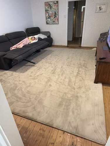 Customer's large, light-colored Mellow Mat covering the wooden floorboards of a living room.