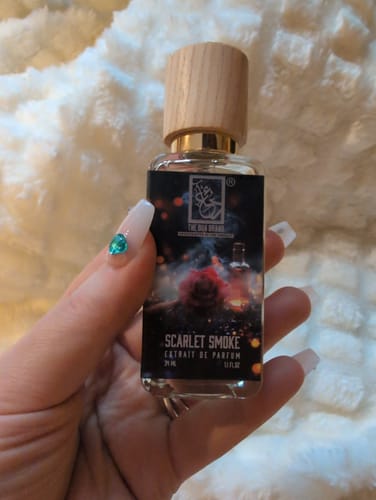 Customer holding the bottle of Scarlet Smoke perfume, showing its wooden cap and detailed label.