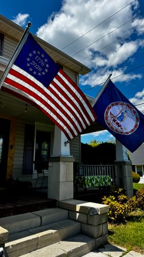 Customer's State of Virginia flag flying from a house porch next to a US flag on a sunny day.