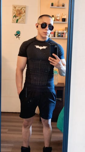 Customer taking a mirror selfie while wearing the fitted black Batman Compression Tee, showing the armored pattern.