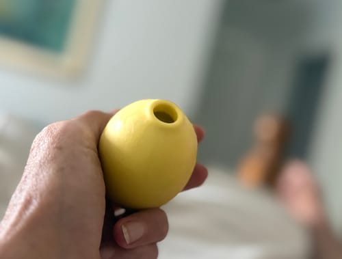 Customer holding the bright, yellow Lem Clitoral Massager in their hand.