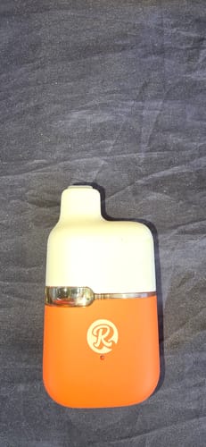 Customer's orange and white 1ML THCA Vape standing on a dark fabric surface.