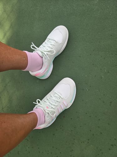 Reviewer wearing the white Express Light Pickleball shoes with pastel accents on a green pickleball court.