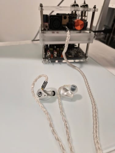 Reviewer's silver CrinEar Reference In-Ear Headphones with a braided cable, shown connected to a tube amplifier.