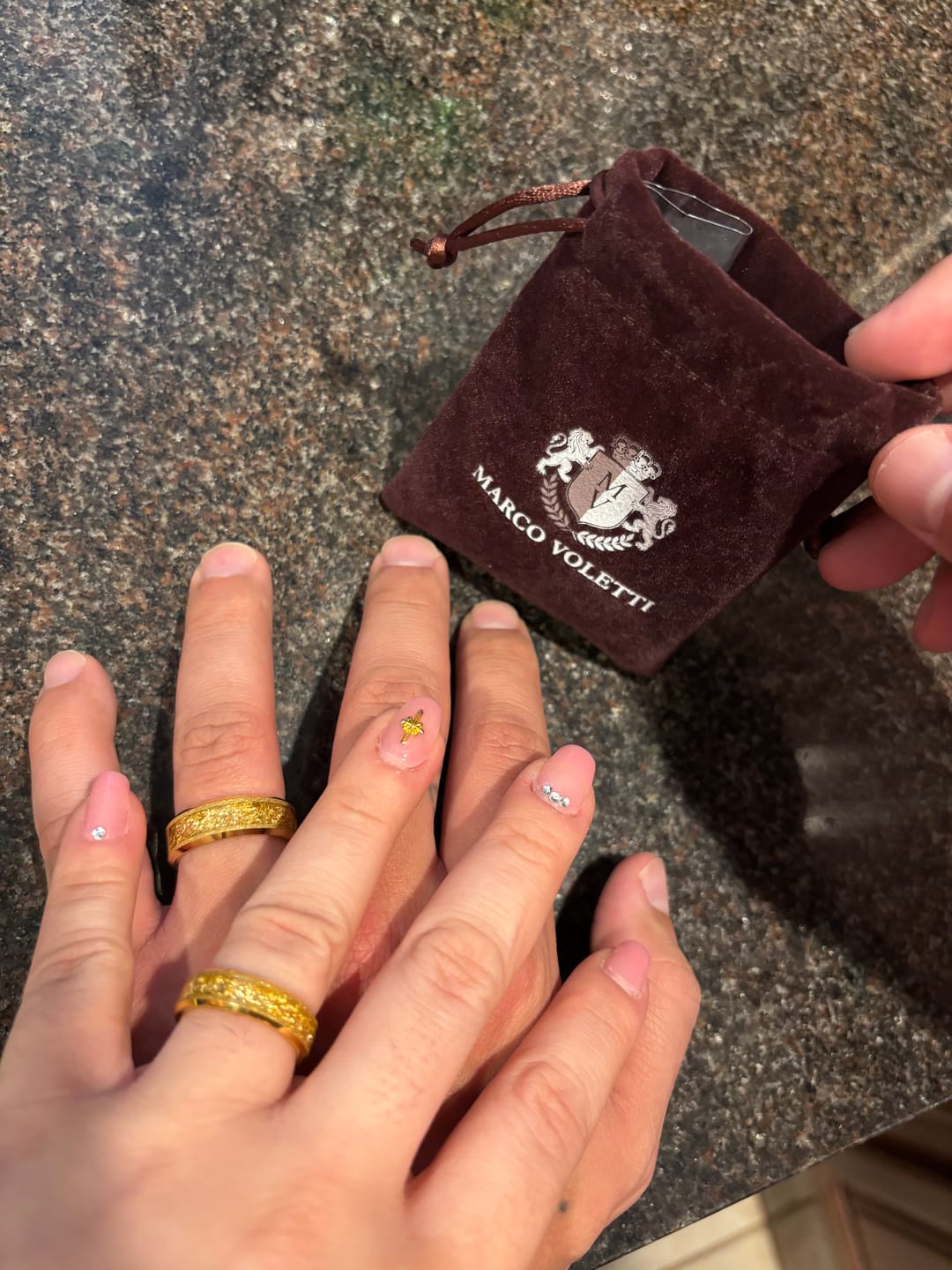 Customer's photo of two intertwined hands, each wearing a textured gold Aureum wedding band.