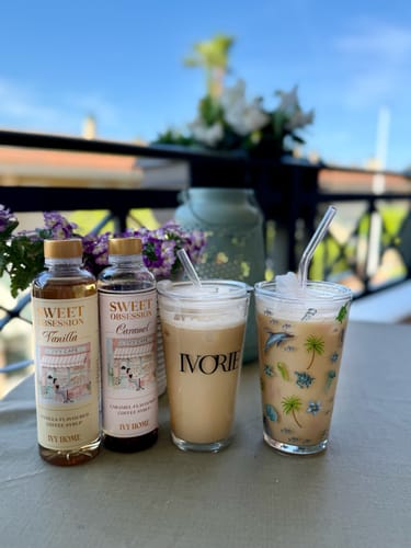 Customer's Sweet Obsession Vanilla Coffee Syrup bottle next to two iced coffees on a sunny outdoor table.