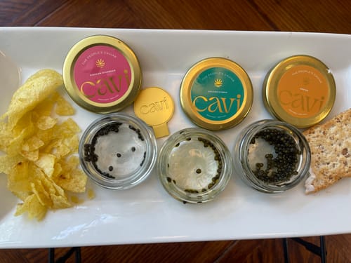 Reviewer's tasting platter with three varieties of caviar in jars and bowls, served with chips and a cracker.