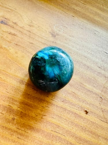 Customer's smooth Labradorite stone showing vibrant blue and green colors on a wood surface.
