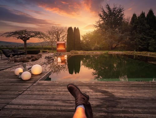 Customer's feet in brown Cognac Tankwa Boots, resting on a wooden deck overlooking a pond at sunset.