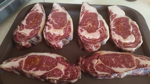 Opinión de cliente de seis filetes Rib Eye Steak Choice crudos en una bandeja marrón.