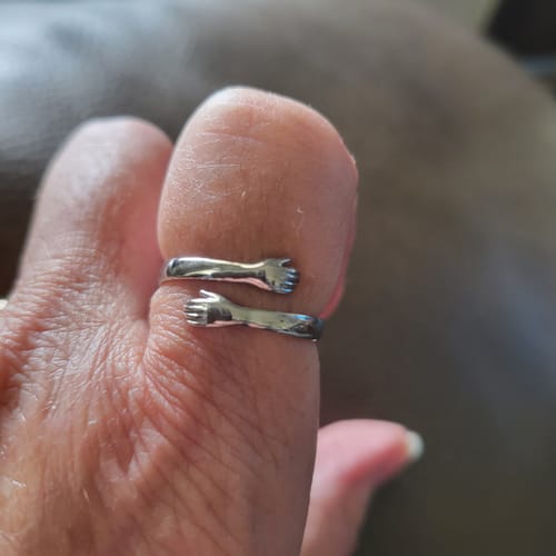 Customer's close-up of the silver Hug From Heaven Ring worn on their thumb, showing the hugging arms design.