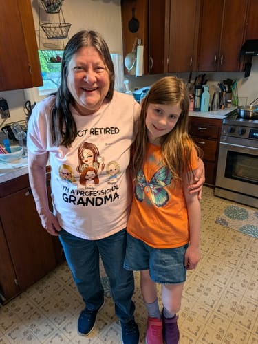 Reviewer smiling while wearing her pink personalized 'I'm a Professional Grandma' shirt and hugging a child.