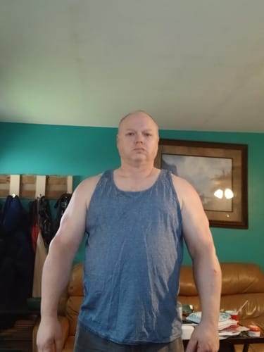 Reviewer in a blue tank top showing his muscular arms and shoulders after using Equi-Mass.
