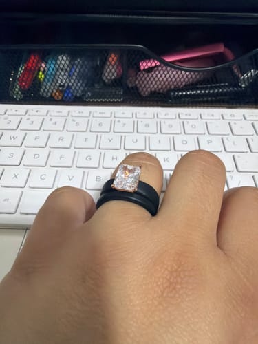 Reviewer's hand showing the black silicone ring with a large emerald-cut stone over a keyboard.