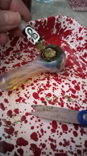Reviewer cutting The Summit pre-roll to pack the flower into a glass pipe.