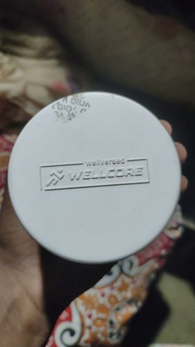 Close-up of a reviewer holding the white container of Wellcore creatine, showing the logo on the lid.