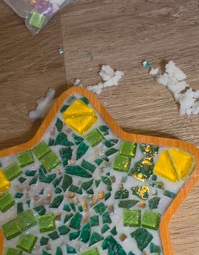 Close-up of a customer's unfinished star-shaped DIY Mosaic Coaster with green and yellow tiles during the grouting process.