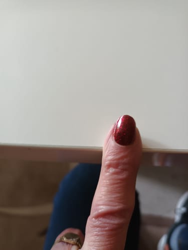 Nahaufnahme des Daumens einer Kundin mit dem glitzernden, roten UV-Gel „Red Sparkle“.