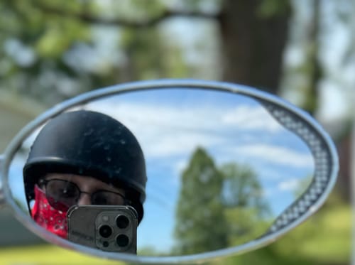 Reviewer's selfie in a motorcycle mirror, showing the low-profile fit of the flat black beanie helmet.
