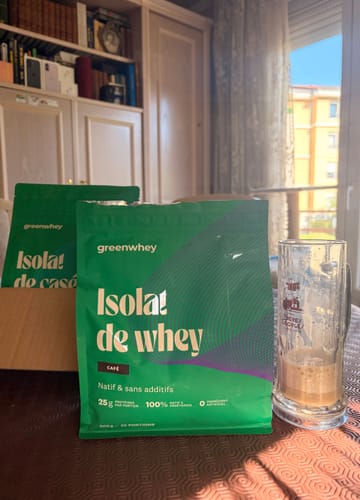 Client montrant son sachet d'Isolat de Whey Native goût café sur une table, à côté d'un verre presque vide.