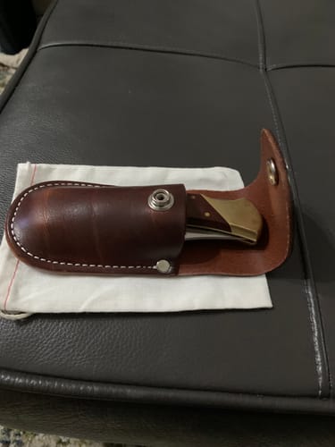 A customer's brown leather Canyon Utility Sheath holding a folded knife. The flap is open, showing the snap.
