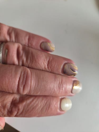 Hand einer Kundin mit einer Maniküre, die das 'Mocha Mousse Marble' UV-Gel-Design mit Goldakzenten zeigt.