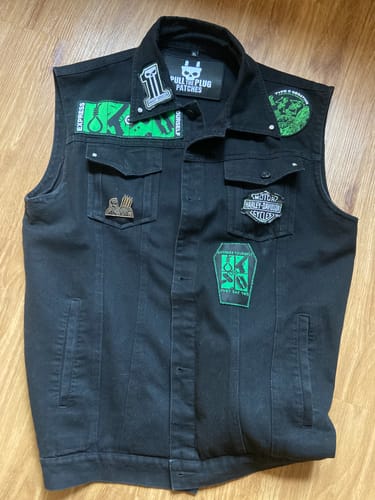 Customer's Left Hand Black Vest laid flat, showing the front decorated with various patches and pins.