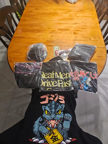 Reviewer's unboxed Cultimate Mystery Cash Box, showing assorted graphic tees and accessories on a wooden table.