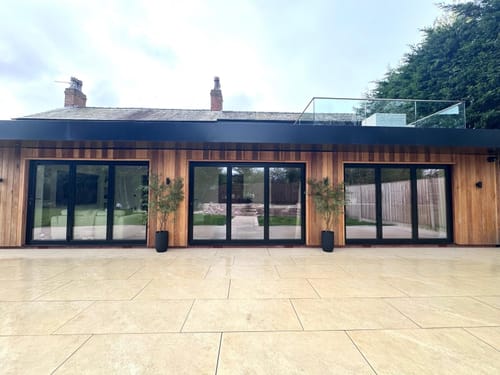 Customer's two Faux Ruscus Trees in black pots on an outdoor patio, flanking glass doors.